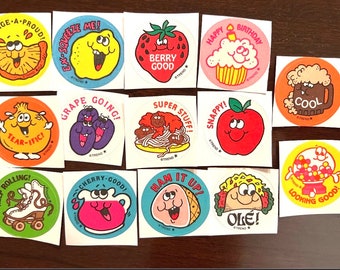 May include: A collection of 12 colorful round stickers with various cartoon characters and phrases. The stickers feature themes like food, fruit, and fun activities. Some of the phrases include "Orange-A-Proud", "Ex-Squeeze Me", "Berry Good", "Happy Birthday", "Grape Going", "Super Stuff", "Snappy", "Tear-ific", "Keep Rolling", "Cherry-Good", "Ham It Up", "Ole", "Cool", and "Looking Good".