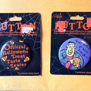May include: Two Halloween-themed buttons on black cards. One button says "Official Halloween Treat Taste Tester" with candy corn graphics. The other features a cartoon Frankenstein and the text "Your patch or mine, Pumpkin?"