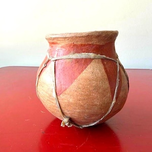 May include: A rounded clay pot with a wide opening, featuring a matte finish in shades of terracotta and tan. The exterior is decorated with large, alternating geometric triangular patterns and is wrapped in thin, light-colored natural fiber cordage.
