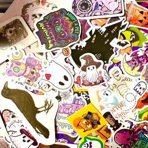 May include: A collection of Halloween themed stickers featuring various designs, including a black cat, a ghost, a skeleton, a haunted house, and a crow. The stickers are colorful and feature a variety of textures and patterns.