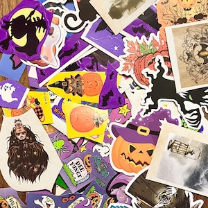 May include: A collection of Halloween themed stickers featuring various designs including pumpkins, ghosts, bats, witches, and a black cat. The stickers are on a wooden surface.