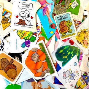 May include: A collection of vintage stickers with various designs. Includes a Snoopy sticker with the text "Thinking of You!", a turtle with the text "Better Late Than Never", and a sticker of an orangutan. Other stickers feature acorns, a ladybug, and a cartoon cow.