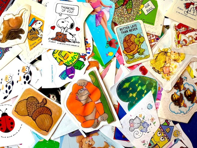Peut inclure: Un assortiment de stickers vintage avec divers motifs. Comprend un autocollant Snoopy avec le texte "Thinking of You!", une tortue avec le texte "Better Late Than Never", et un autocollant d'orang-outan. D'autres autocollants pr&eacute;sentent des glands, une coccinelle et une vache de dessin anim&eacute;.