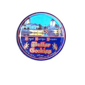 May include: A white ceramic mug with a black handle and the text "But First, Coffee" in a bold, black font. The mug is set against a blurred background, suggesting a cozy setting.