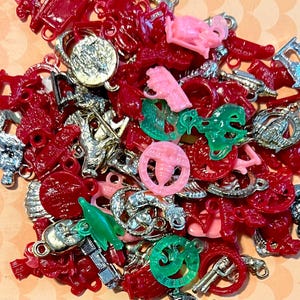 May include: A collection of colorful plastic charms in red, green, pink, and silver. The charms feature various designs, including animals, hearts, and stars.