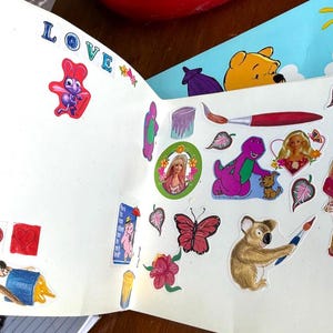 May include: A collection of colorful stickers featuring various designs, including cartoon characters like Winnie the Pooh, Barney, and Barbie. Other stickers include a monkey, flowers, and stars. The word "LOVE" is visible.