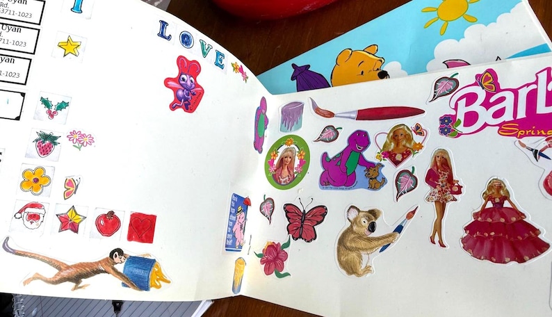 May include: A collection of colorful stickers featuring various designs, including cartoon characters like Winnie the Pooh, Barney, and Barbie. Other stickers include a monkey, flowers, and stars. The word "LOVE" is visible.