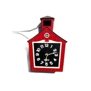 May include: A red, house-shaped clock with a black clock face and white numbers. The clock has a small, square tower on top and a white cord. The clock's hands point to 2:15. The clock is a vintage style.