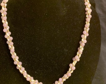May include: A delicate necklace featuring a double strand of light pink and white beads. The necklace is displayed on a black velvet mannequin.