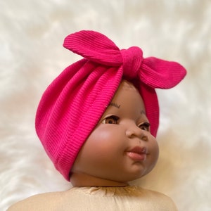 May include: A pink turban headband with a bow on top. The headband is made of a soft, stretchy fabric and is perfect for newborns and babies.