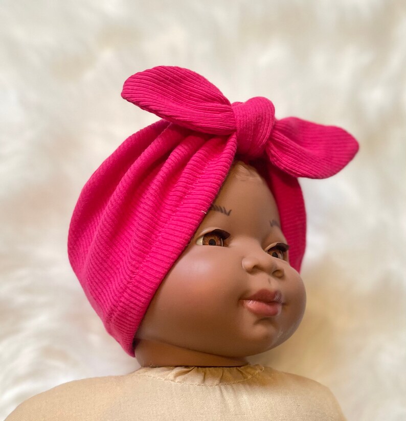 May include: A pink turban headband with a bow on top. The headband is made of a soft, stretchy fabric and is perfect for newborns and babies.