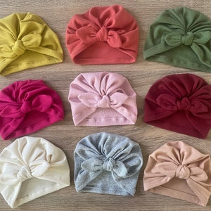 May include: Assortment of ten turban headbands in various colors, including mustard yellow, red, olive green, pink, burgundy, beige, and gray. Each headband features a knotted bow on top.