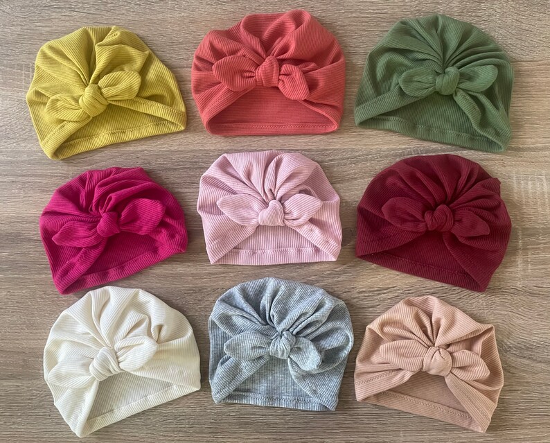 May include: Assortment of ten turban headbands in various colors, including mustard yellow, red, olive green, pink, burgundy, beige, and gray. Each headband features a knotted bow on top.