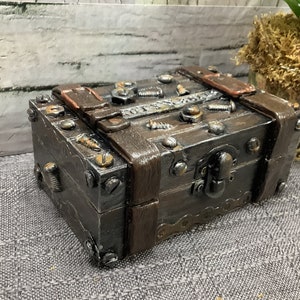 May include: A small wooden box with a metal latch and hinges. The box is decorated with screws and other metal accents. The box is brown and has a rustic look.