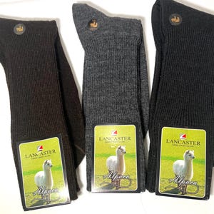 May include: Three pairs of alpaca socks in brown, gray, and black. Each pair has a tag with the brand name "Lancaster" and an image of an alpaca. The tag also says "Alpaca" in a decorative font.