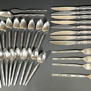 Könnte beinhalten: Ein Besteckset mit silbernem Finish. Das Set enthält 18 Teile: 12 Löffel, 4 Gabeln und 2 Messer. Die Griffe des Bestecks sind mit einem sich wiederholenden Muster aus Quadraten verziert.