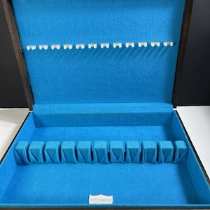 May include: Open wooden silverware storage box with a blue felt interior. The box has slots for utensils along the top and bottom, with a small label that reads "ANTI-TARNISH". The box is designed to protect silverware.