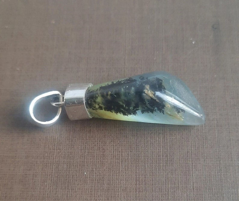 May include: A silver pendant with a green, black, and white agate stone. The stone is shaped like a teardrop and has a silver bail.