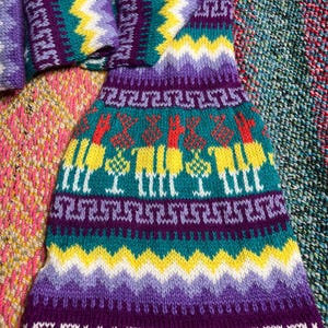 Könnte beinhalten: Ein gestrickter Schal in Lila, Grün, Gelb und Weiß mit geometrischem Muster und dem Wort "PERU" am unteren Rand.