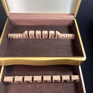 May include: Open wooden cutlery storage box with a light brown interior and a dark brown lining. The box is labelled "COMMUNITY THE FINEST SILVERPLATE" on the inside lid. The box has two levels with slots for cutlery.