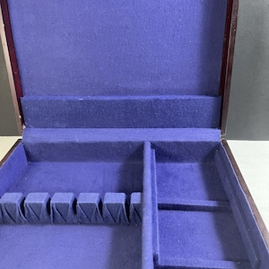 May include: Open wooden silverware storage box with a dark purple felt interior. The box has compartments for utensils and a hinged lid. The exterior is a dark brown color.