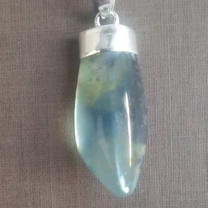 May include: A silver pendant with a light blue and green gemstone. The gemstone is a teardrop shape and has a smooth, polished finish.