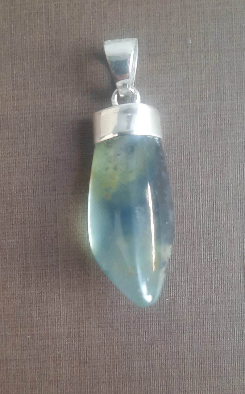 May include: A silver pendant with a light blue and green gemstone. The gemstone is a teardrop shape and has a smooth, polished finish.