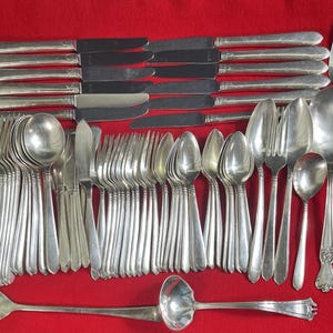 Puede incluir: Un conjunto completo de cubiertos antiguos, que incluye tenedores, cuchillos, cucharas y utensilios para servir, dispuestos sobre un fondo rojo. La cubertería de metal plateado incluye tenedores, cuchillos y cucharas de varios tamaños y estilos.