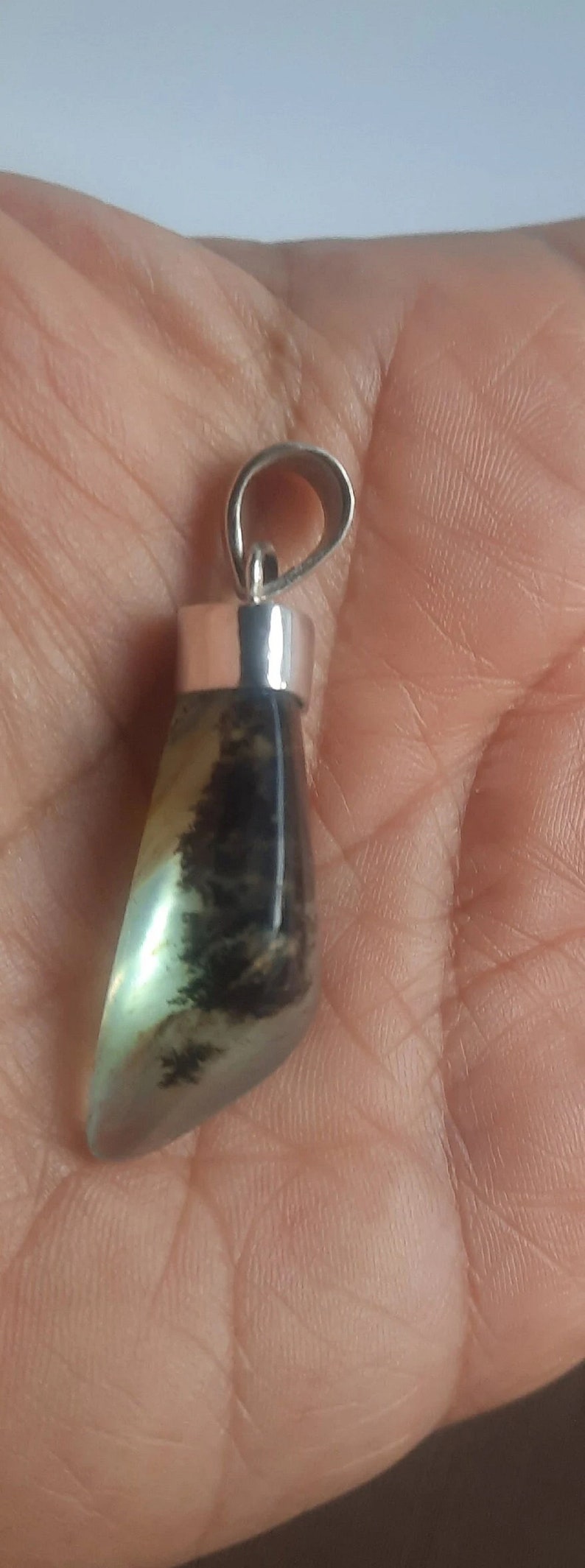 May include: A silver pendant with a green and black agate stone. The stone is a teardrop shape and has a silver bail.