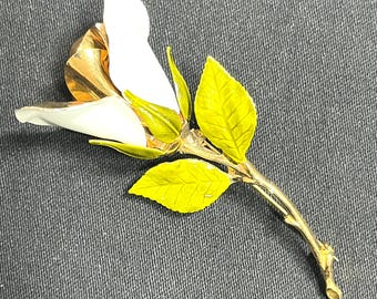 May include: A white enamel rose brooch with gold-tone leaves and stem. The rose is stylized and has a single, large petal.