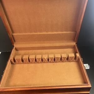 May include: Open wooden silverware storage box with a brown felt interior. The box is rectangular with a hinged lid and a series of slots for utensils. The exterior is a dark wood finish with brass-colored hardware.
