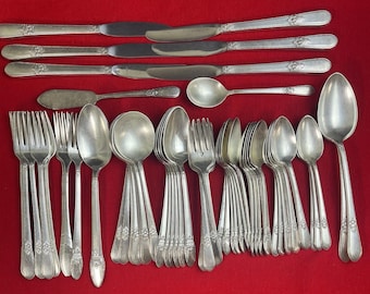 Può includere: Una collezione di posate d'epoca, tra cui forchette, cucchiai e coltelli, disposte su una superficie rossa. Le posate hanno un motivo floreale sui manici. Il set comprende cucchiai e forchette di varie dimensioni, coltelli da burro e coltelli da tavola.