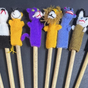 May include: A set of eight knitted animal finger puppets attached to wooden sticks. The puppets include a yellow and black striped tiger, a white and black panda, a yellow bear, a purple cat, a yellow lion with a mane, a blue creature, a white and brown animal, and a black cat.