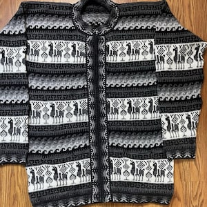 May include: A full-length, zip-up sweater in shades of gray, black, and white. The sweater features a repeating pattern of llamas and geometric shapes. The collar is a crew neck style. The sweater is made of a thick, woven material.
