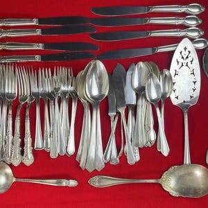 Peut inclure: Une collection d'argenterie ancienne, comprenant des couteaux, des fourchettes, des cuillères et des ustensiles de service. Les couverts argentés sont disposés sur une surface rouge. L'ensemble comprend des fourchettes, des cuillères et des couteaux de différentes tailles et styles, ainsi que des pièces de service.