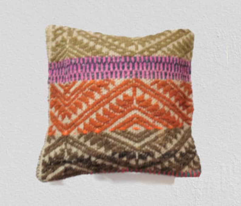 Peut inclure: Un coussin carr&eacute; avec un motif tiss&eacute; color&eacute;. Le coussin a un fond blanc avec des rayures brunes, orange, roses et vertes et des motifs g&eacute;om&eacute;triques.