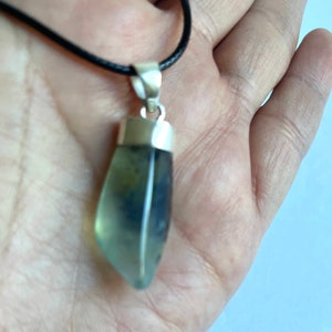 May include: A silver pendant with a light green and blue gemstone on a black cord.