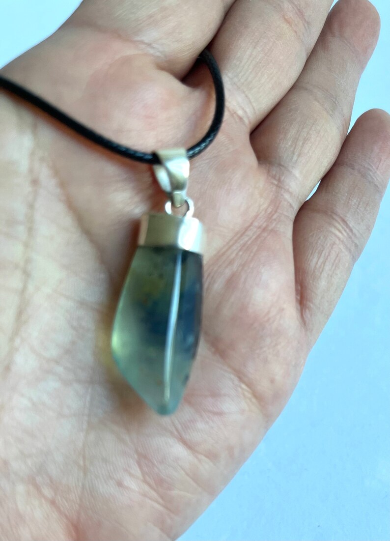 May include: A silver pendant with a light green and blue gemstone on a black cord.