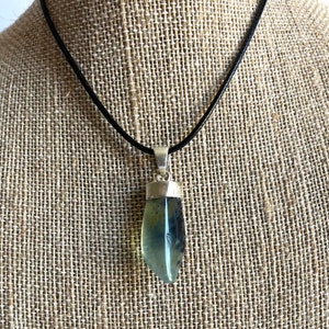 May include: A silver pendant with a green and blue gemstone on a black leather cord.