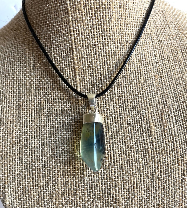 May include: A silver pendant with a green and blue gemstone on a black leather cord.