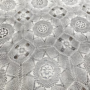 May include: Cream-colored, crocheted tablecloth featuring a repeating floral pattern. The intricate design showcases detailed openwork and a delicate, textured surface. The overall aesthetic is vintage and handmade, suitable for a dining table.