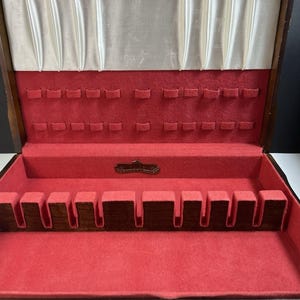 May include: Open wooden silverware storage box with a red felt interior and a cream-colored satin lining. The box has slots for utensils and a small metal plate that reads "Harmony House".