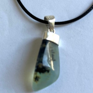 May include: A silver pendant necklace with a light green and black agate stone. The stone is set in a silver bezel and hangs from a black cord.