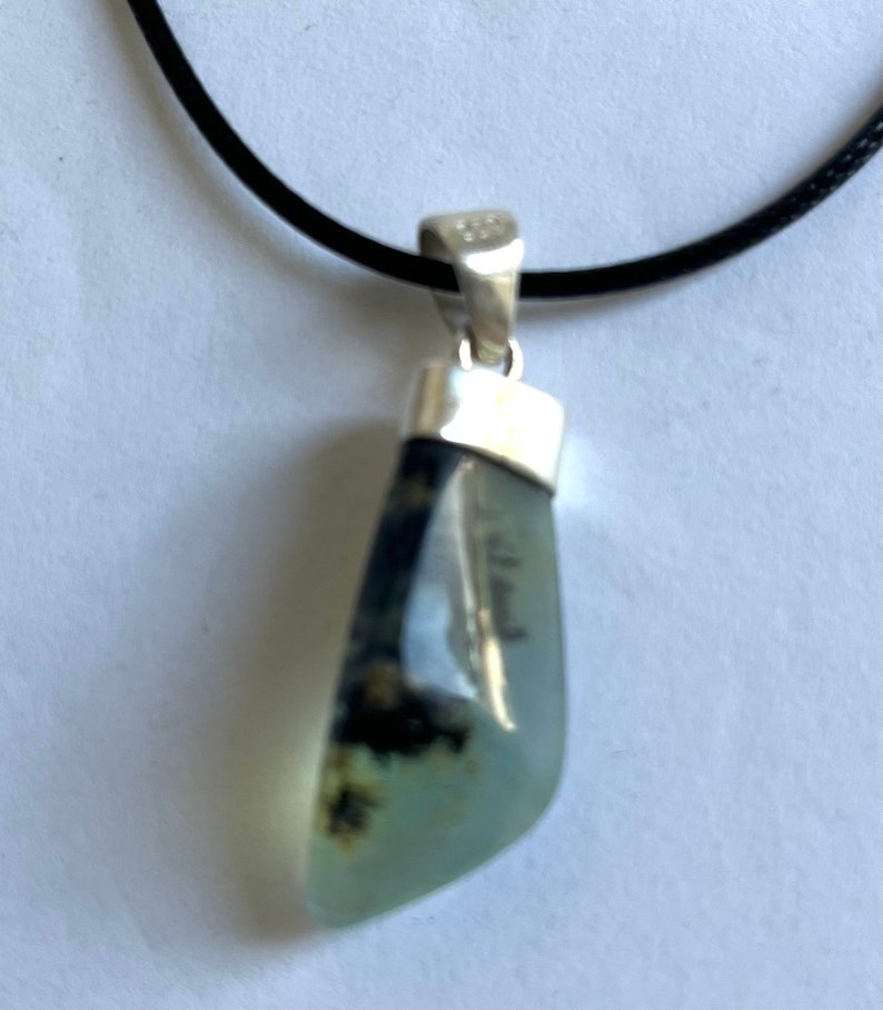 May include: A silver pendant necklace with a light green and black agate stone. The stone is set in a silver bezel and hangs from a black cord.