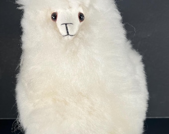 May include: White fluffy alpaca plush toy with brown eyes and ears. The toy is standing on a black surface.