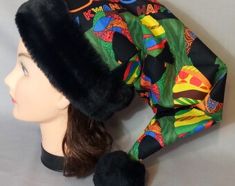May include: A long, black Kwanzaa hat with a black faux fur trim and a black pom-pom. The hat features a colorful African print with the words "KWANZAA HAPPY" in red and yellow.