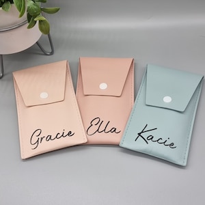 May include: Three small, personalised gift bags with a flap and button closure. The bags are in shades of pink and blue and are labelled "Gracie", "Ella", and "Kacie".