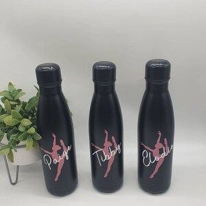 May include: Three black stainless steel water bottles with pink and white dancer silhouettes and personalized names: Paige, Tibby, and Elodie.