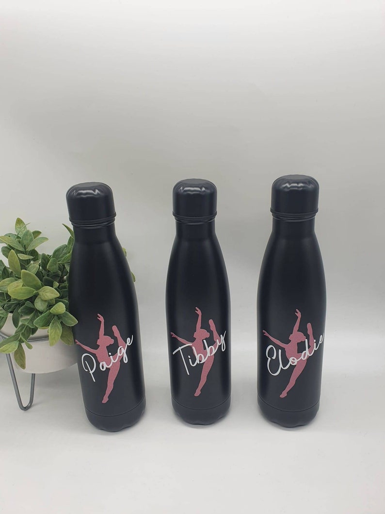 May include: Three black stainless steel water bottles with pink and white dancer silhouettes and personalized names: Paige, Tibby, and Elodie.