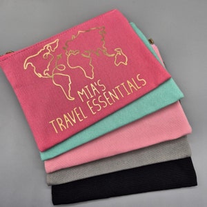 May include: A stack of five pink, green, grey, and black zippered pouches with a gold outline of a world map and the text "MIA'S TRAVEL ESSENTIALS" on the top pouch.